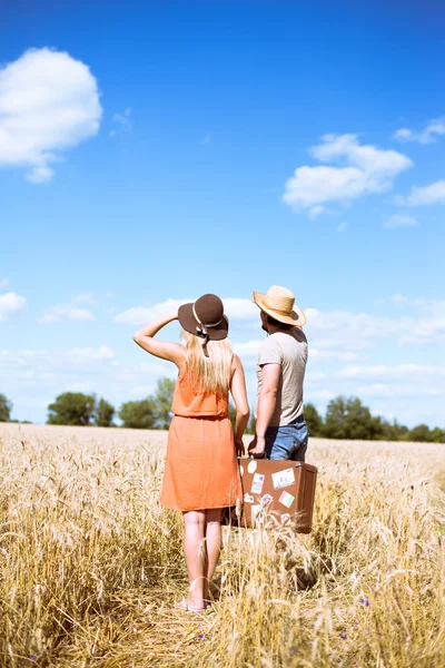Happy couple standing with old suitcase on sunny countryside background