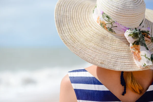 Backview of elegant young woman in straw hat on oceanside