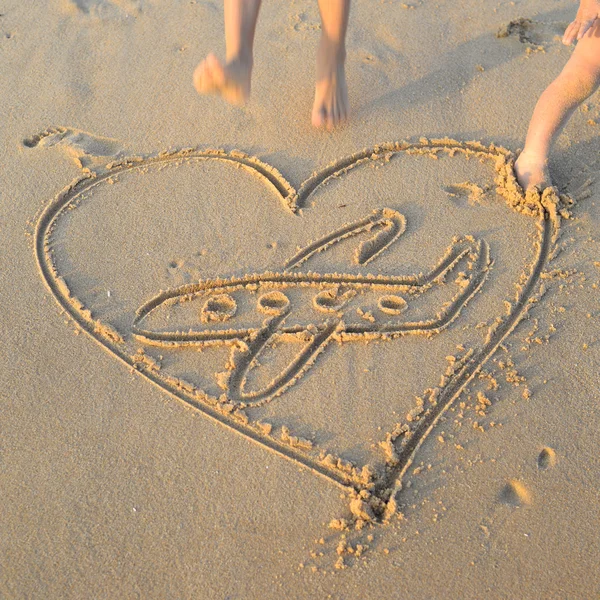 Closeup of heart and plane handwritten on golden seaside sand