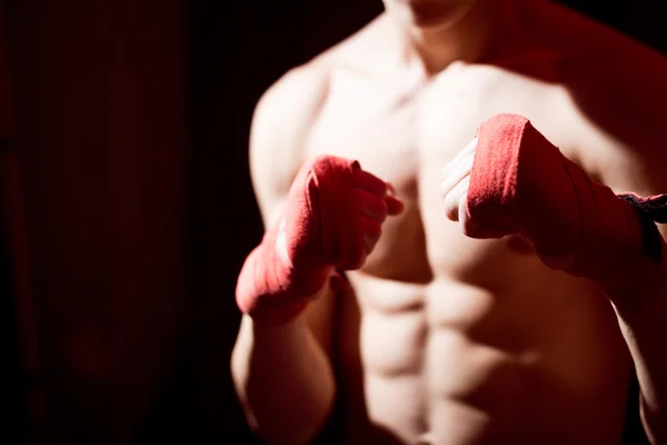 Male training box punches with bandages closeup on strong muscles of torso over dark background. Boxing workout.