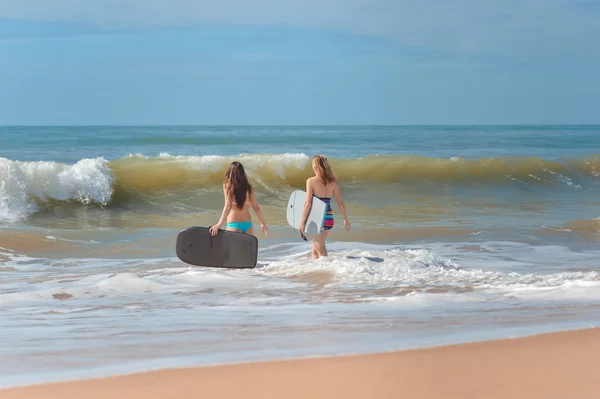 Back view of beautiful young women with surfboards entering sea