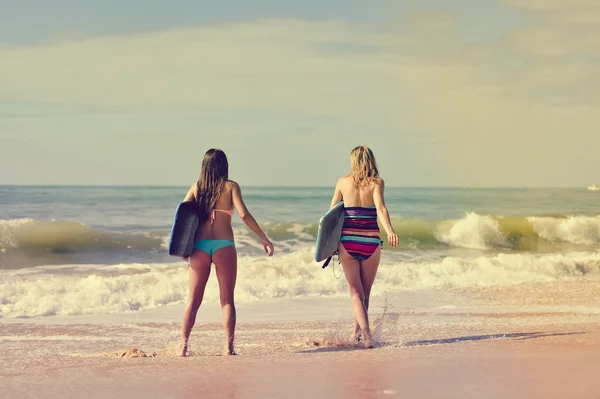 Back view of beautiful young women walking away with surfboards