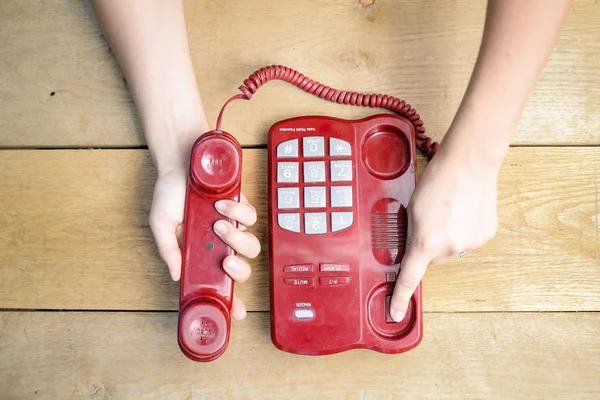 Closeup of female hands ending conversation by red cord telephone