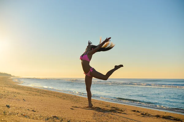 Picture of beautiful young lady in pink bikini dancing on seaside beach. Pretty girl with long hair on sunny summer outdoor background.