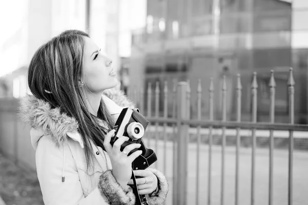 Beautiful young lady holding photo camera on city glass building background. Black white photography