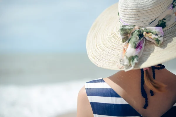 Back view of elegant beautiful woman in dress and straw hat on the beach.