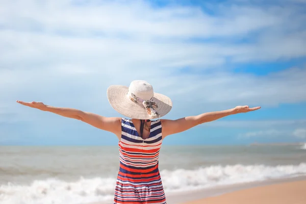 Back view of romantic lady enjoying summer beach and sun, waving at sea. Concept of feeling and freedom