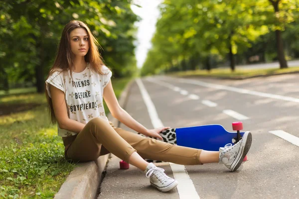 Very beautiful young girl with long hair sitting in the park on the track and keep lorgbord. Skateboarding. lifestyle