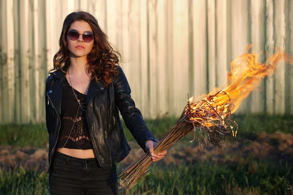 Young girl with glasses and a bully black jacket holding the torch outdoors