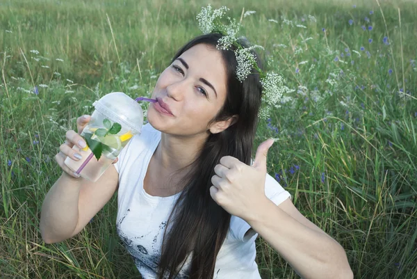 Beautiful young woman on nature background, drink water with lemon and mint