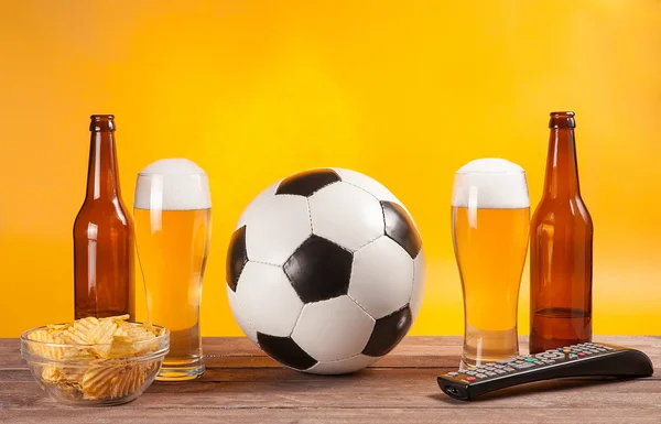 Glass with beer and soccer ball near tv remote