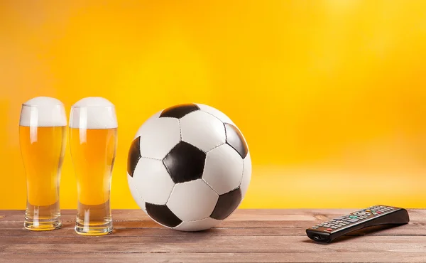 Two glasses beer and soccer ball near tv remote