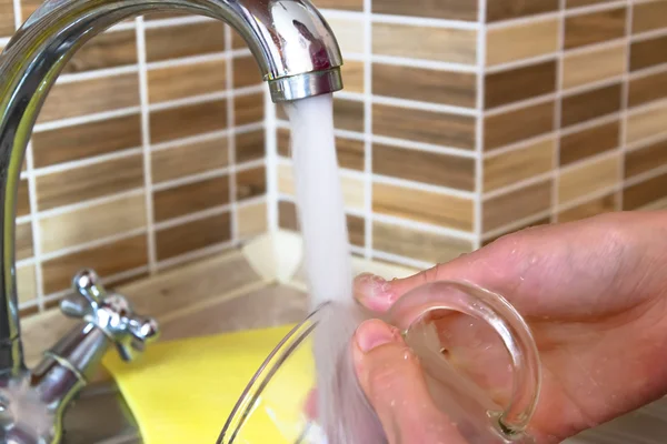 Woman washes a transparent Cup under the tap in the kitchen