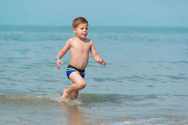 Little boy child running through the sea with is tongue out