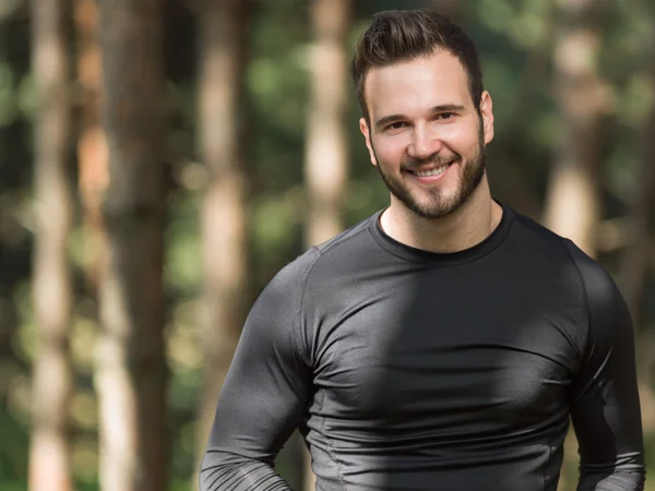 Smiling handsome muscular young man standing outdoors in a woode