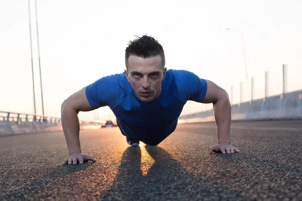 Handsome male runner doing push-ups on stairs in urban setting,