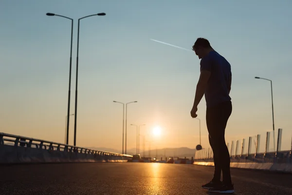 Attractive fit man running fast along big modern bridge at sunse