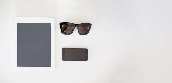 Tablet computer, mobile phone and sunglasses on a wooden table