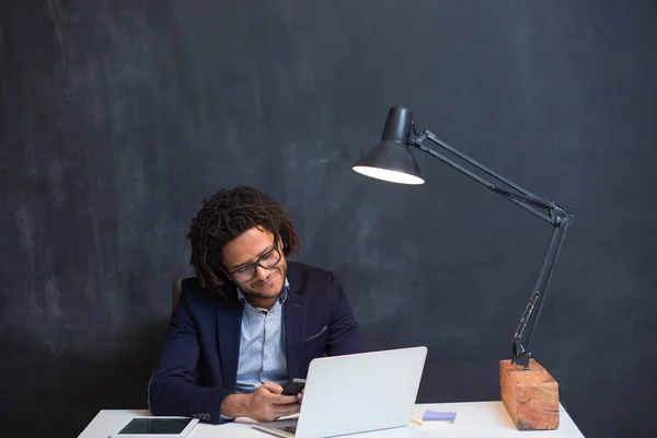 Portrait of happy smart black businessman sitting at desk in off