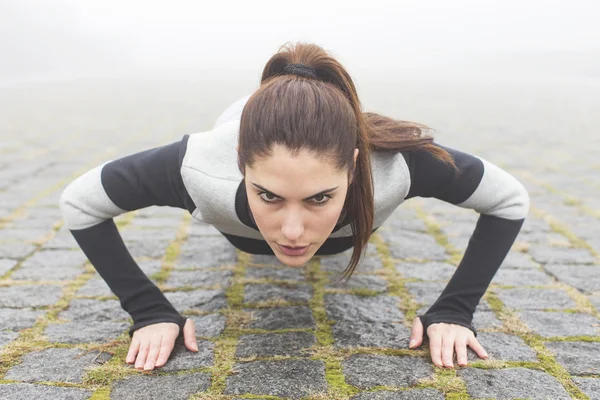 Young female athlete doing push-ups on a foggy day.