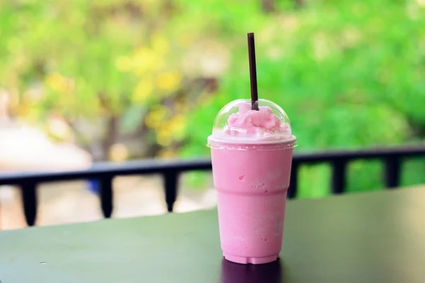 Pink milk shake on wooden table on geen background