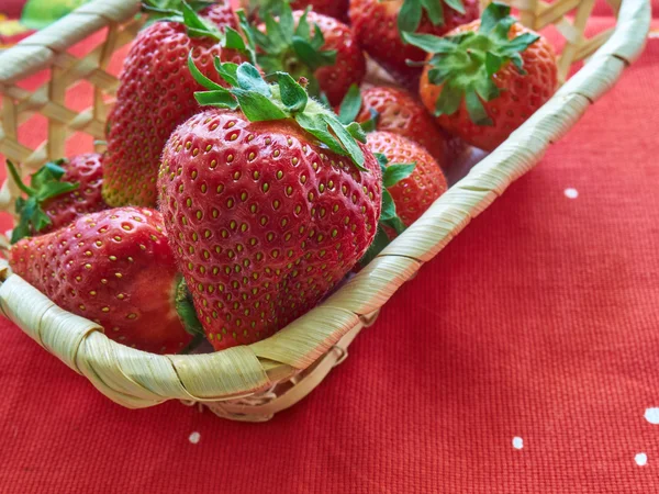 Large strawberries in a wicker basket, a small wicker basket stands on a red napkin