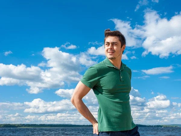 Young man wearing polo looking away at the beach under scenic cloudy sky on sunny day