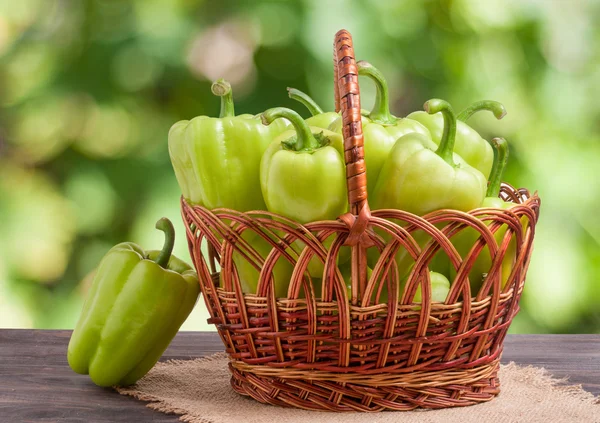 Green bell peppers in a wicker basket on  wooden table with  blurred background