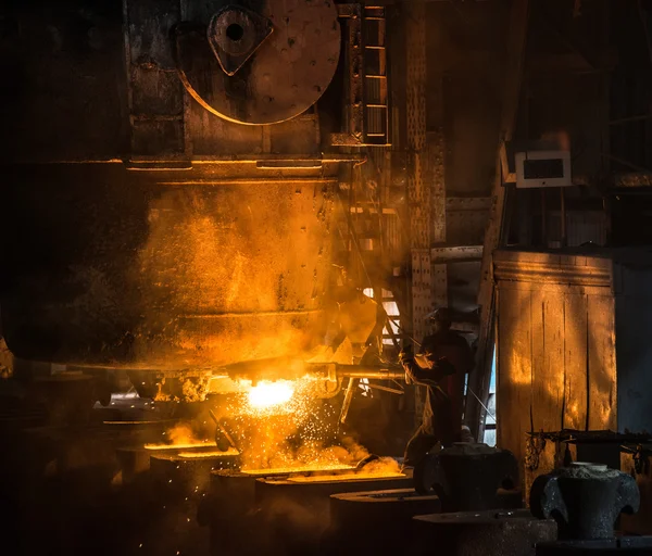 Steelworker pours liquid metal into molds from tank