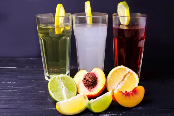 Three fruits soft-drinks with lemon on a edge of a glass. Lime, lemon and peach on a bottom on a dark background.