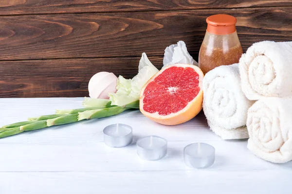 Composition of spa treatment on white wooden background with grapefruit, gladiolus, towels, bath bomb and candles. With copy space