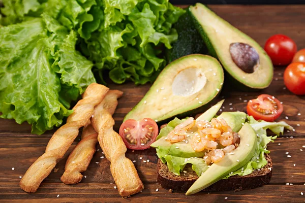 Rye bread sandwich with shrimp, avocado, tomatoes and breadsticks