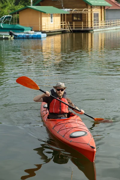 Man boating in red canoe at river pier at summer day