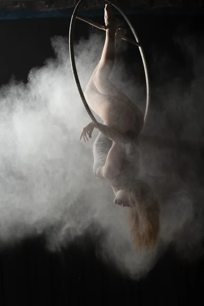 Acrobatic woman doing gymnastic element on aerial hoop with sprinkled flour