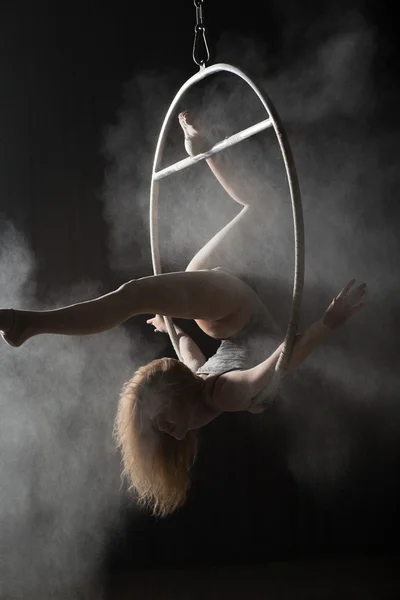 Female acrobat doing gymnastic twine on aerial hoop with sprinkled flour