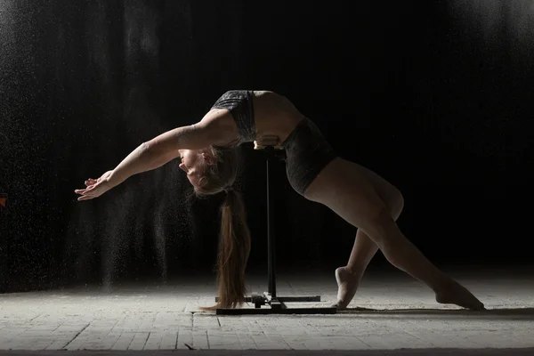 Woman doing gymnastic element on stand while sprinkled flour