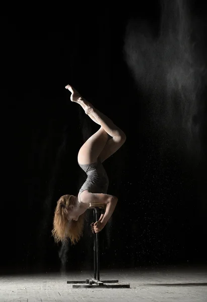 Woman gymnast handstand on equilibre at black background