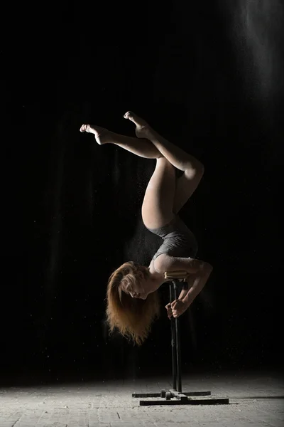 Woman gymnast handstand on equilibre at black background