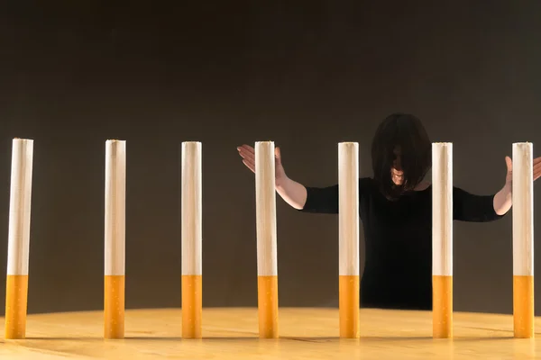 Woman standing behind a row of cigarettes as a concept of a prisoner of the addiction having in smoking.