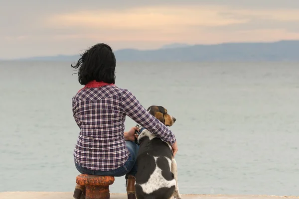 Woman and her dog against the sea watching the sunset.