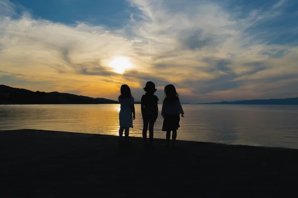 Three little girls watching the sunset against a dramatic sky.