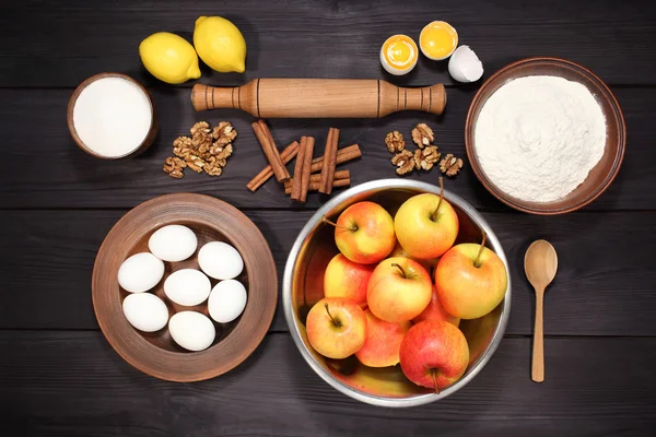 Products and ingredients for making homemade apple pie, spread out on a rustic table in a plates and bowls