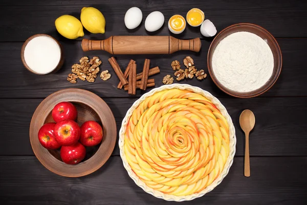 Products and ingredients for making homemade apple pie, spread out on a rustic table in a plates and bowls