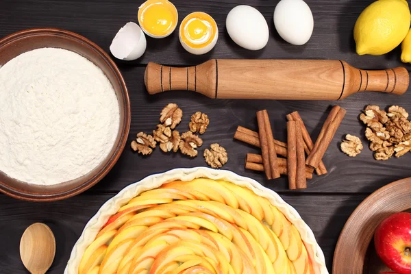 Products and ingredients for making homemade apple pie, spread out on a rustic table in a plates and bowls