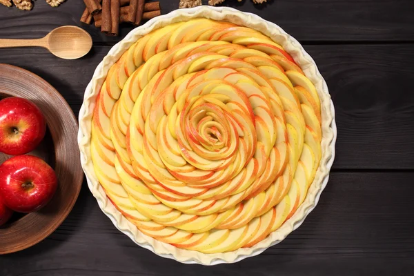 Products and ingredients for making homemade apple pie, spread out on a rustic table in a plates and bowls