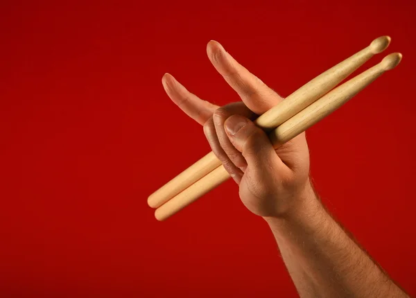 Man hand with drumsticks and devil horns over red