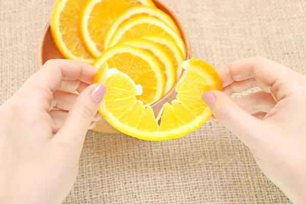 Fruit in a wooden bowl in her hand torn orange, ready for consum,fruit of juicy ripe orange in a wooden plate exposed to nice illustrations of  orange,her  hand holds the slice of orange taken  from a wooden plate, on the background of burlap spinnin