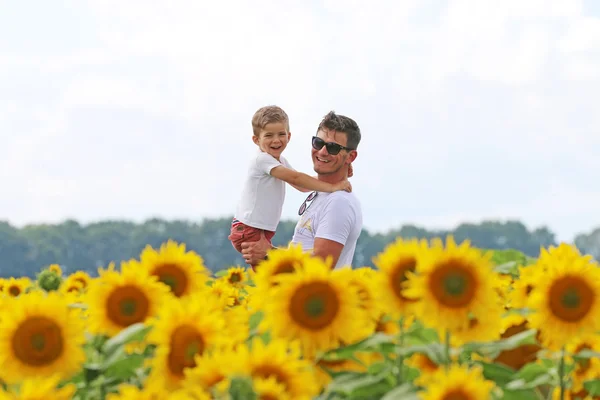 Happy joyfull father with his cute clever well mannered  son in field of blossoming sunflower