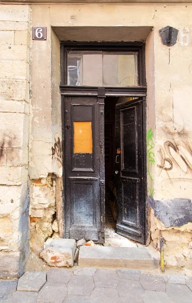 Old black open doors into the entrance, there is graffiti on the walls