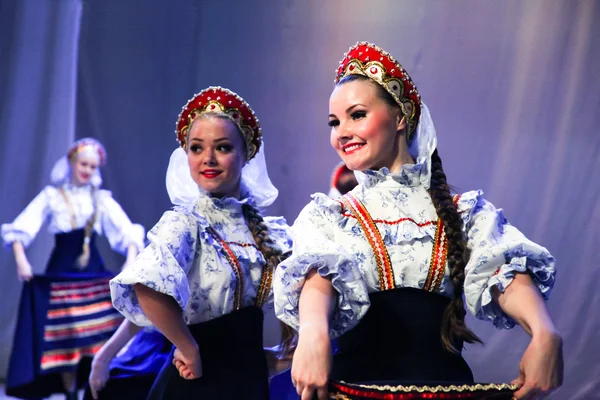A group of girls in sundresses dancing Russian folk dance and smiling